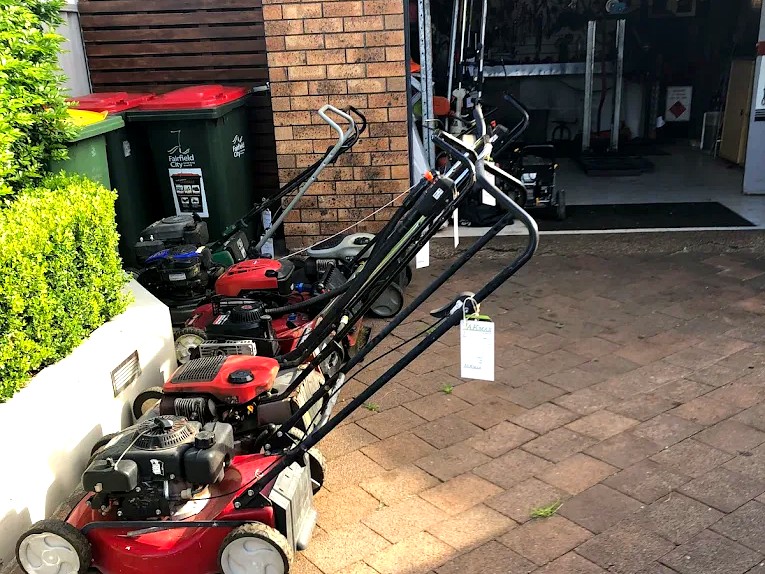 A row of lawn mowers lined up outside John's workshop in Fairfield, ready for service